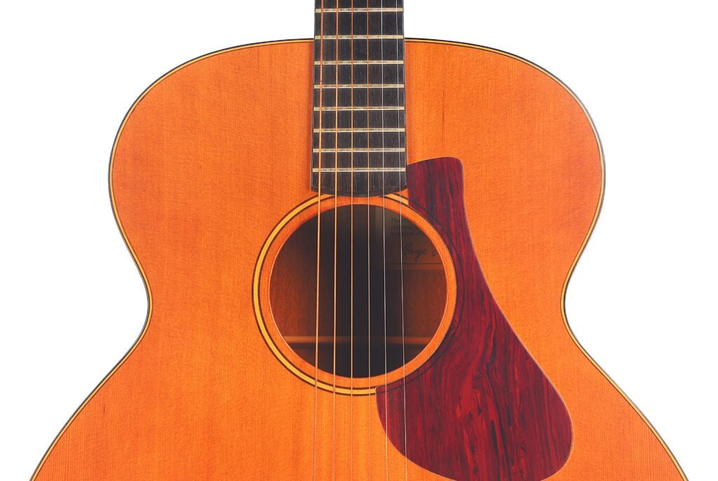 Nahaufnahme des Korpus der Lowden S-5 Akustik Gitarre. Hervorzuheben sind die Saiten, das Schallloch, das Griffbrett und das rotbraune Schlagbrett vor einem weißen Hintergrund. Nahaufnahme des Korpus der Lowden S-5 Akustik Gitarre. Hervorzuheben sind die Saiten, das Schallloch, das Griffbrett und das rotbraune Schlagbrett vor einem weißen Hintergrund.