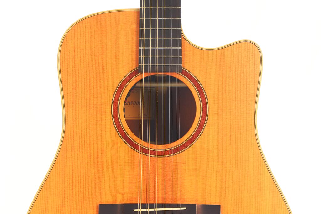 Nahaufnahme der Lakewood D-14-12 Cut 2005 Akustik Gitarre mit Holzkorpus, rundem Schallloch mit Zierring und einem Teil des Griffbretts vor weißem Hintergrund. Nahaufnahme der Lakewood D-14-12 Cut 2005 Akustik Gitarre mit Holzkorpus, rundem Schallloch mit Zierring und einem Teil des Griffbretts vor weißem Hintergrund.