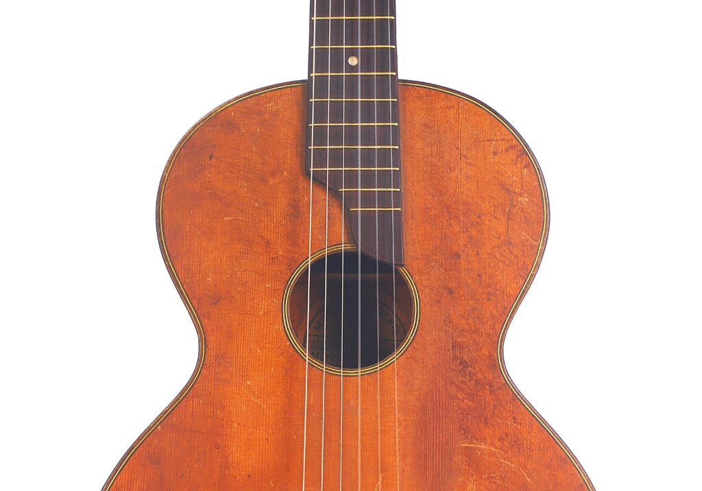 Nahaufnahme des Korpus und des Halses der Braun & Hauser 1905 Klassische Gitarre, die die warme braune Holzoberfläche, die sichtbaren Saiten und die Oberflächenabnutzung zeigt. Nahaufnahme des Korpus und des Halses der Braun & Hauser 1905 Klassische Gitarre, die die warme braune Holzoberfläche, die sichtbaren Saiten und die Oberflächenabnutzung zeigt.