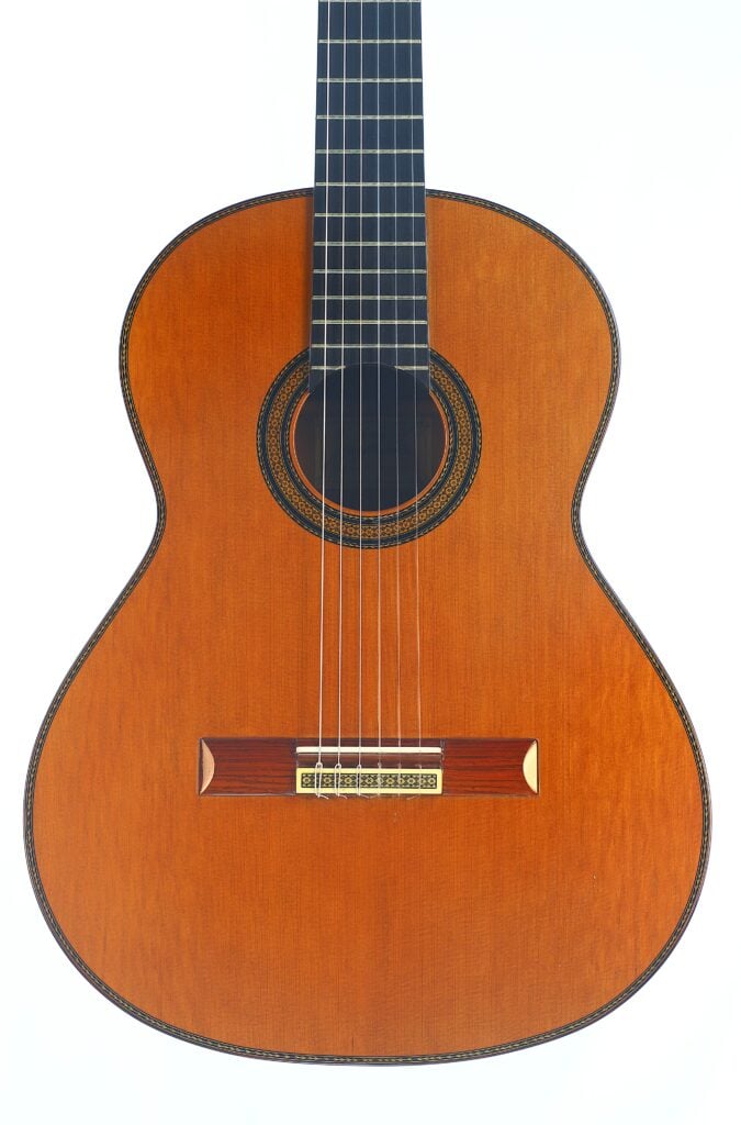 Die klassische Gitarre „Manuel Contreras 1981 Doble Tapa“ ist eine sechssaitige klassische Akustikgitarre mit naturbelassener Holzoberfläche, rundem Schallloch und dekorativer Rosette, die vor einem weißen Hintergrund abgebildet ist. Die klassische Gitarre „Manuel Contreras 1981 Doble Tapa“ ist eine sechssaitige klassische Akustikgitarre mit naturbelassener Holzoberfläche, rundem Schallloch und dekorativer Rosette, die vor einem weißen Hintergrund abgebildet ist.