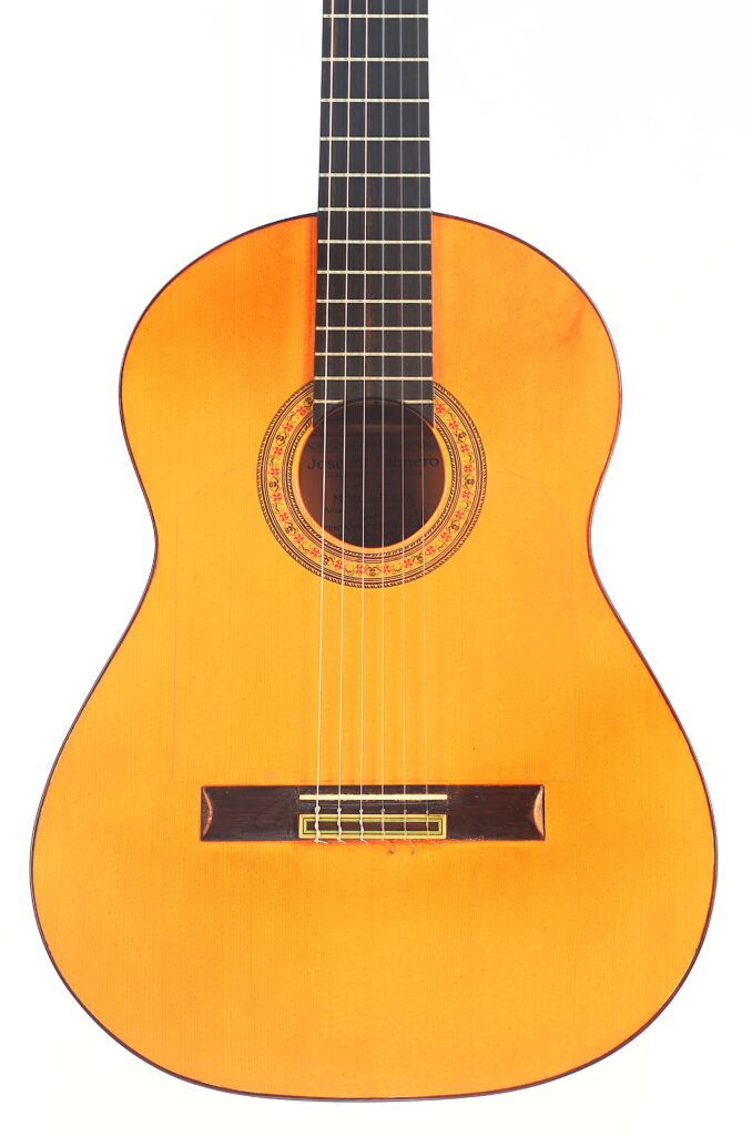 Die Flamenco-Gitarre „José M Palmero 2023“ verfügt über einen hellen Holzkorpus, ein dunkles Griffbrett, sechs Saiten und eine dekorative Rosette am Schallloch, die sich vor einem weißen Hintergrund abhebt. Die Flamenco-Gitarre „José M Palmero 2023“ verfügt über einen hellen Holzkorpus, ein dunkles Griffbrett, sechs Saiten und eine dekorative Rosette am Schallloch, die sich vor einem weißen Hintergrund abhebt.