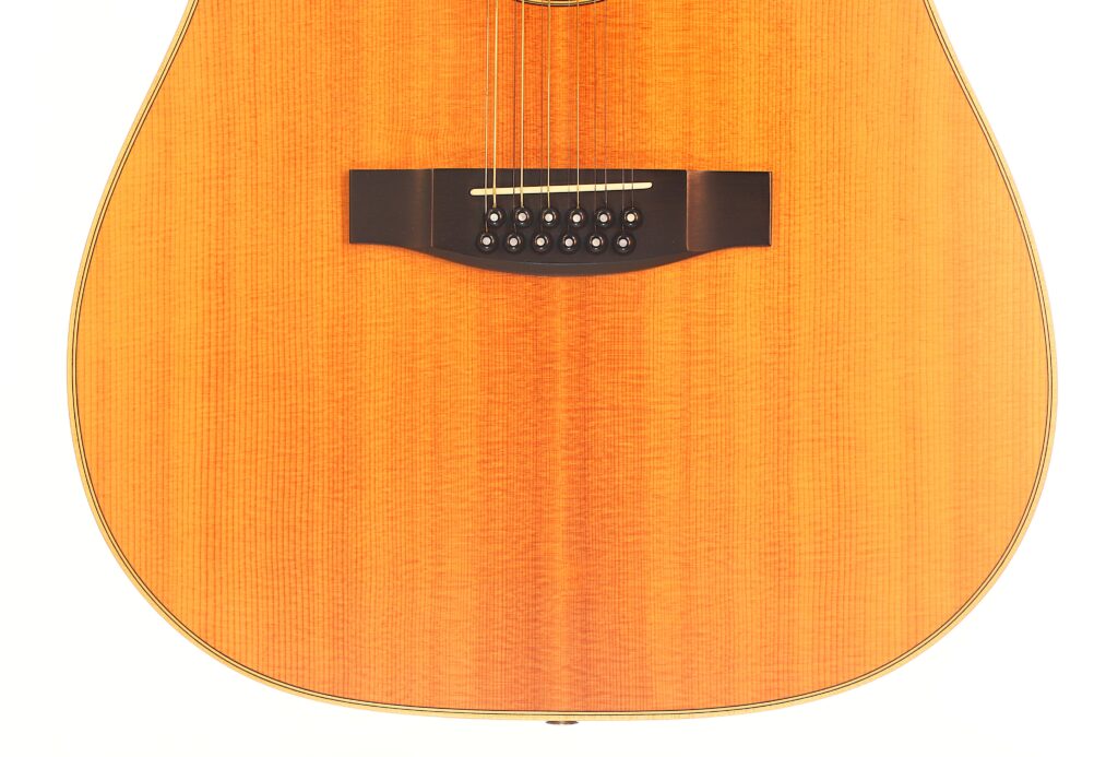 Nahaufnahme des Naturholzkorpus der Lakewood D-14-12 Cut 2005 Akustik Gitarre, die den Steg, die Saiten und den Resonanzboden vor einem weißen Hintergrund hervorhebt. Nahaufnahme des Naturholzkorpus der Lakewood D-14-12 Cut 2005 Akustik Gitarre, die den Steg, die Saiten und den Resonanzboden vor einem weißen Hintergrund hervorhebt.