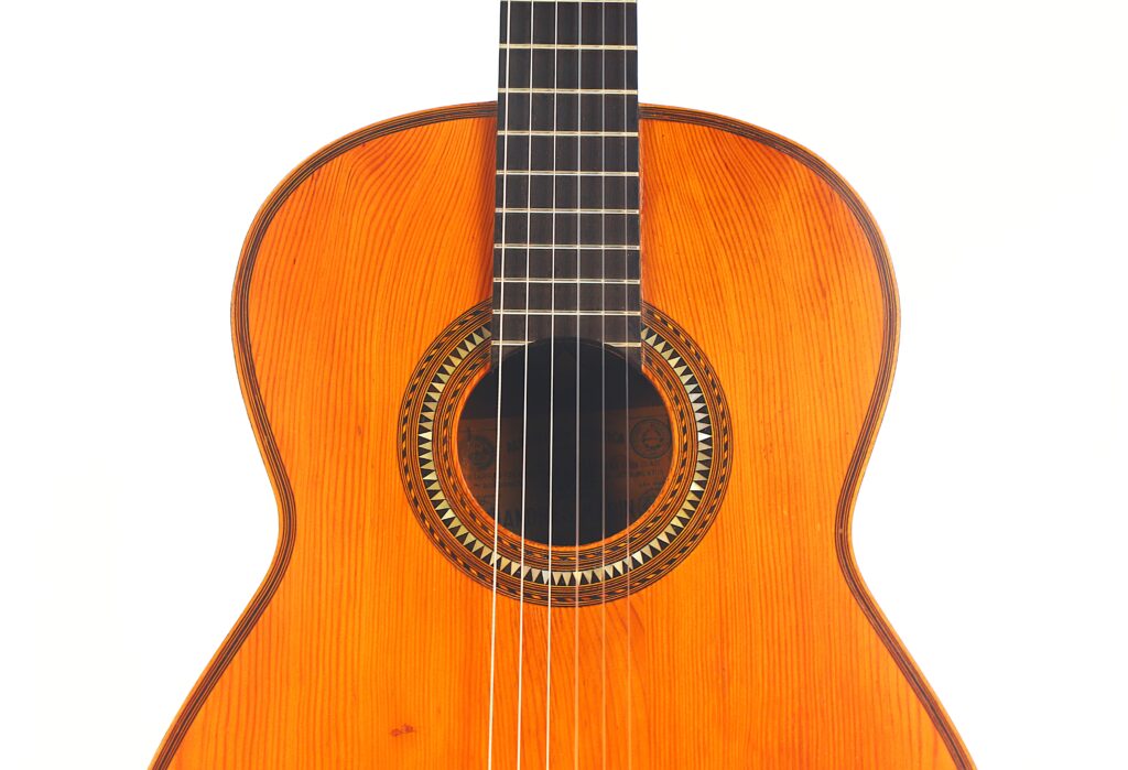 Eine Nahaufnahme der Andres Marin 1900 Klassische Gitarre, die den hölzernen Korpus und die Saiten zeigt, mit Schwerpunkt auf dem Schallloch und einem Teil des Griffbretts, vor einem weißen Hintergrund. Eine Nahaufnahme der Andres Marin 1900 Klassische Gitarre, die den hölzernen Korpus und die Saiten zeigt, mit Schwerpunkt auf dem Schallloch und einem Teil des Griffbretts, vor einem weißen Hintergrund.