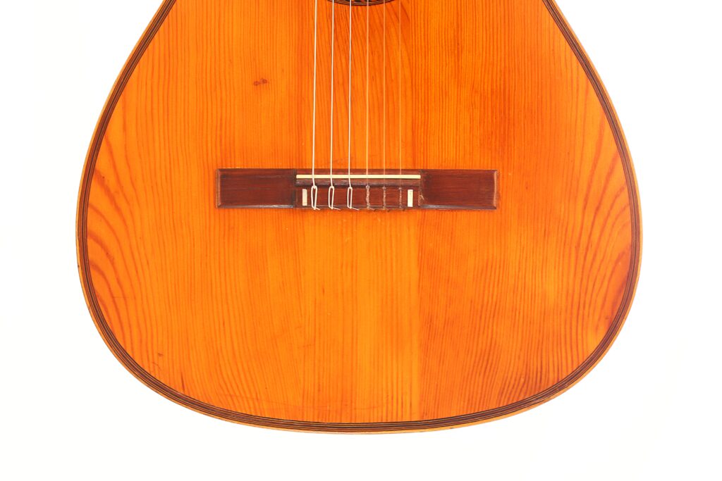 Nahaufnahme des Korpus der Andres Marin 1900 Klassische Gitarre, wobei die Saiten, der Steg und die feine Holzmaserung vor einem weißen Hintergrund hervorgehoben werden. Nahaufnahme des Korpus der Andres Marin 1900 Klassische Gitarre, wobei die Saiten, der Steg und die feine Holzmaserung vor einem weißen Hintergrund hervorgehoben werden.