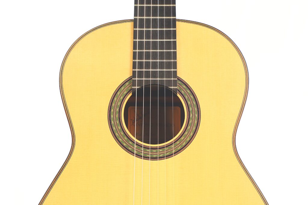 Nahaufnahme der Vorderseite des Korpus und der Saiten der Antonio Aparicio Mod. Master Klassische Gitarre. Hervorzuheben ist das Schallloch mit dekorativer Einlage vor weißem Hintergrund. Nahaufnahme der Vorderseite des Korpus und der Saiten der Antonio Aparicio Mod. Master Klassische Gitarre. Hervorzuheben ist das Schallloch mit dekorativer Einlage vor weißem Hintergrund.