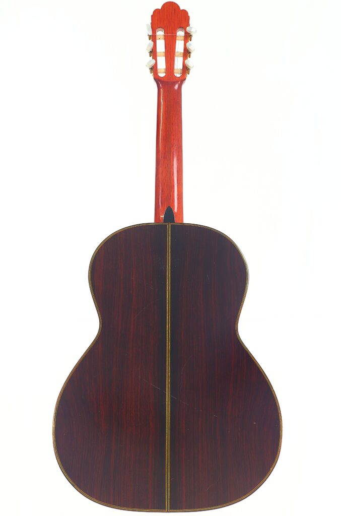 Rückansicht einer Juan Estruch Chet Atkins Yellow Label 1976 Klassische Gitarre, einer klassischen Akustikgitarre mit dunklem Holzkorpus, sichtbarer Mittelnaht sowie rötlichem Hals und Kopfplatte, vor weißem Hintergrund. Rückansicht einer Juan Estruch Chet Atkins Yellow Label 1976 Klassische Gitarre, einer klassischen Akustikgitarre mit dunklem Holzkorpus, sichtbarer Mittelnaht sowie rötlichem Hals und Kopfplatte, vor weißem Hintergrund.