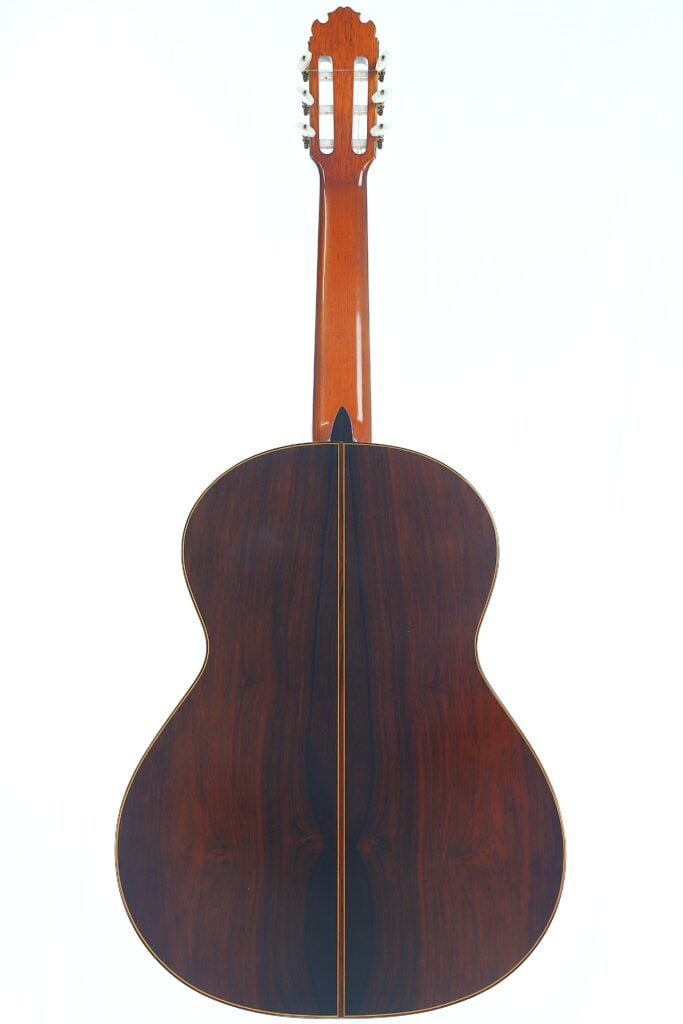 Rückansicht einer „Doble Tapa Klassische Gitarre“ von Manuel Contreras aus dem Jahr 1981 mit einem glänzenden, dunklen Holzboden, einem hellbraunen Hals und sichtbaren Stimmwirbeln, alles vor einem weißen Hintergrund. Rückansicht einer „Doble Tapa Klassische Gitarre“ von Manuel Contreras aus dem Jahr 1981 mit einem glänzenden, dunklen Holzboden, einem hellbraunen Hals und sichtbaren Stimmwirbeln, alles vor einem weißen Hintergrund.