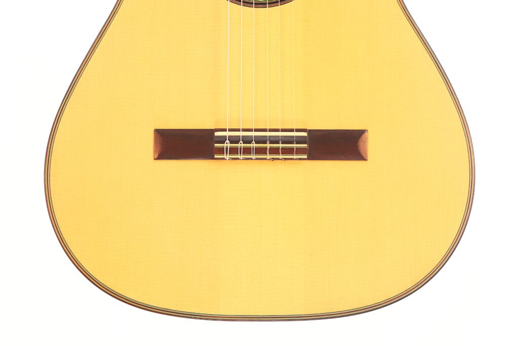 Nahaufnahme des Korpus der Antonio Aparicio Mod. Master Klassische Gitarre mit hellem Holzkorpus, einem dunklen Holzsteg und sechs Saiten. Nahaufnahme des Korpus der Antonio Aparicio Mod. Master Klassische Gitarre mit hellem Holzkorpus, einem dunklen Holzsteg und sechs Saiten.