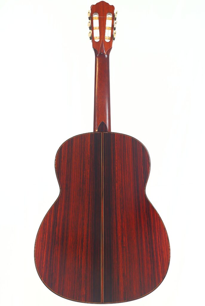 Das Bild zeigt die Rückseite einer „Klassische Gitarre“ von Joachim Schneider aus dem Jahr 1977 mit einer polierten, dunkelrotlichen Holzoberfläche und einer sichtbaren Mittelnaht vor weißem Hintergrund. Das Bild zeigt die Rückseite einer „Klassische Gitarre“ von Joachim Schneider aus dem Jahr 1977 mit einer polierten, dunkelrotlichen Holzoberfläche und einer sichtbaren Mittelnaht vor weißem Hintergrund.