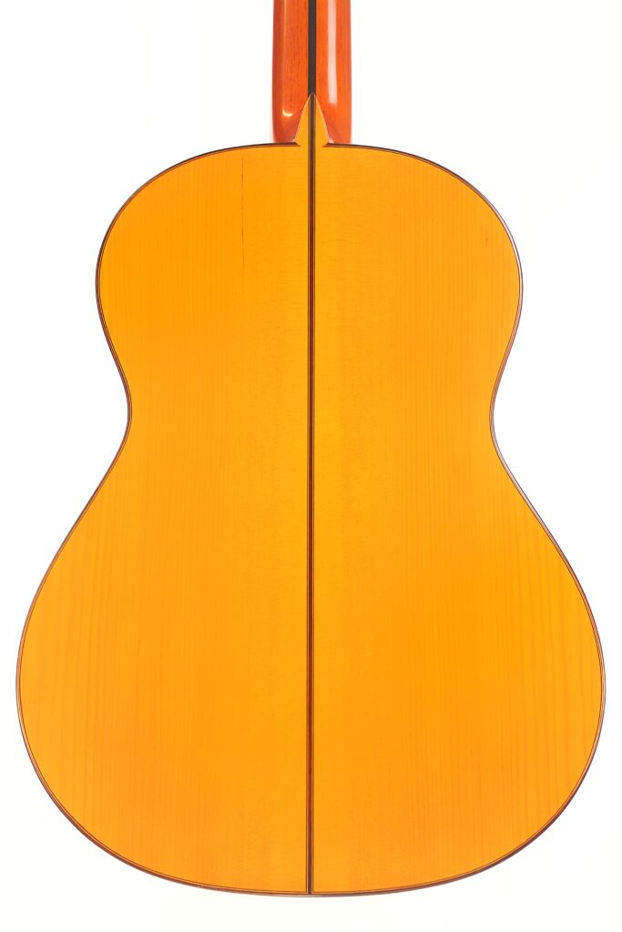 Das Bild zeigt die Rückseite einer Juan Montero 1993 Blanca Flamenco Gitarre mit einer hellen Holzoberfläche und einer dunklen vertikalen Naht in der Mitte vor einem weißen Hintergrund. Das Bild zeigt die Rückseite einer Juan Montero 1993 Blanca Flamenco Gitarre mit einer hellen Holzoberfläche und einer dunklen vertikalen Naht in der Mitte vor einem weißen Hintergrund.
