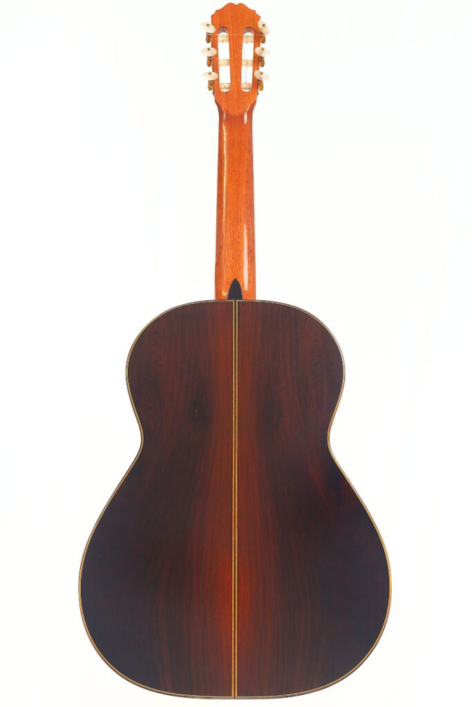 Die Antonio Aparicio Mod. Master Klassische Gitarre wird von der Rückseite gezeigt, wobei der reiche dunkle Holzkorpus mit einer zentralen dekorativen Einlage und einem hellbraunen Hals hervorgehoben wird, alles vor einem weißen Hintergrund. Die Antonio Aparicio Mod. Master Klassische Gitarre wird von der Rückseite gezeigt, wobei der reiche dunkle Holzkorpus mit einer zentralen dekorativen Einlage und einem hellbraunen Hals hervorgehoben wird, alles vor einem weißen Hintergrund.