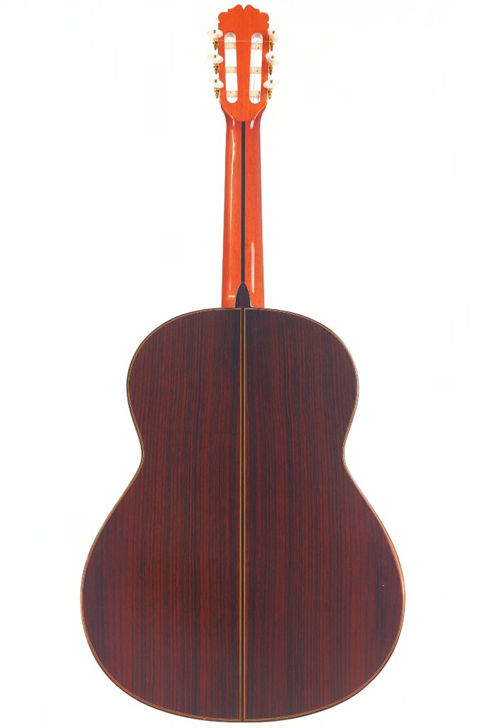 Die Juan Miguel Gonzalez 2006 Klassische Gitarre ist von hinten abgebildet und zeigt ihren dunklen Holzkorpus mit einer zentralen Einlage und einem rötlichen Hals und einer Kopfplatte vor einem weißen Hintergrund. Die Juan Miguel Gonzalez 2006 Klassische Gitarre ist von hinten abgebildet und zeigt ihren dunklen Holzkorpus mit einer zentralen Einlage und einem rötlichen Hals und einer Kopfplatte vor einem weißen Hintergrund.