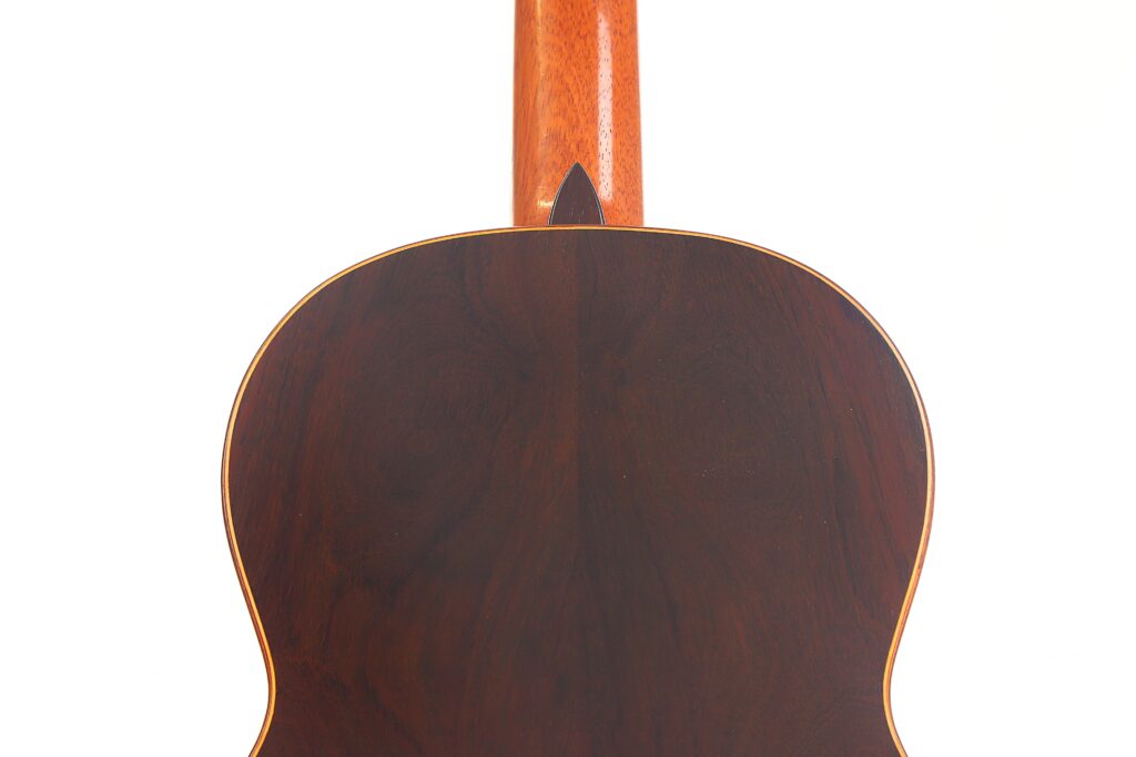 Rückansicht der „Carl Hermann Schäfer – Nicolaus Wollf 2012 Klassische Gitarre“ mit einem Korpus aus dunklem Holz, einem unteren Hals und einer hellen Kantenumrandung, abgebildet vor weißem Hintergrund. Rückansicht der „Carl Hermann Schäfer – Nicolaus Wollf 2012 Klassische Gitarre“ mit einem Korpus aus dunklem Holz, einem unteren Hals und einer hellen Kantenumrandung, abgebildet vor weißem Hintergrund.