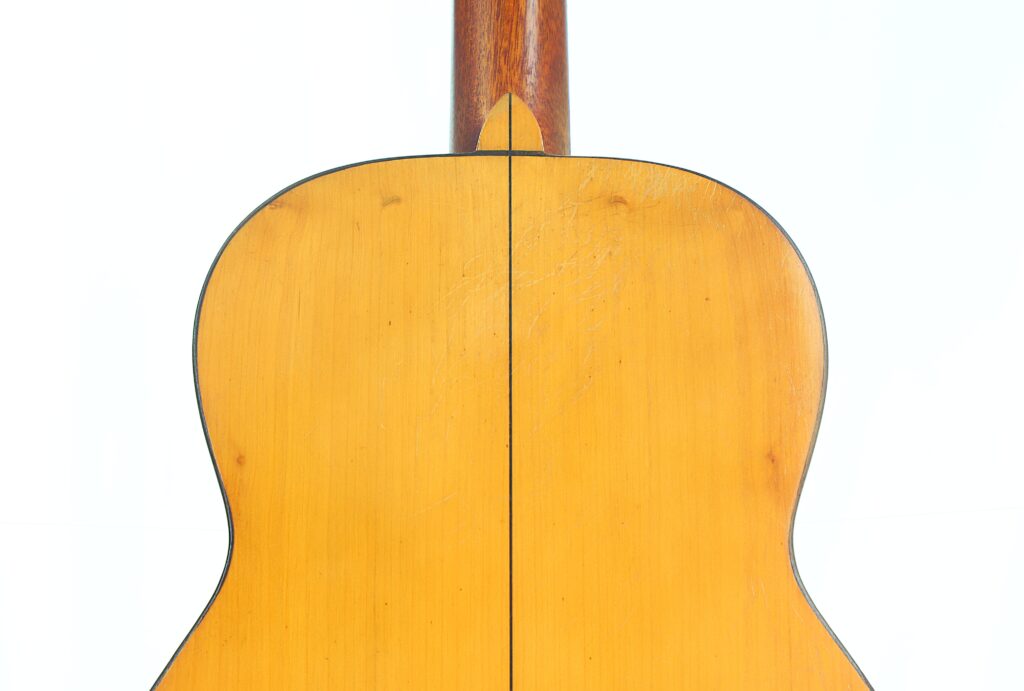 Nahaufnahme der Rückseite einer „Jose Ramirez I 1921“ Klassischen Gitarre, die sich durch helles Holz mit einer sichtbaren Mittelnaht auszeichnet; der Halsansatz ist im oberen Bildbereich zu sehen. Nahaufnahme der Rückseite einer „Jose Ramirez I 1921“ Klassischen Gitarre, die sich durch helles Holz mit einer sichtbaren Mittelnaht auszeichnet; der Halsansatz ist im oberen Bildbereich zu sehen.