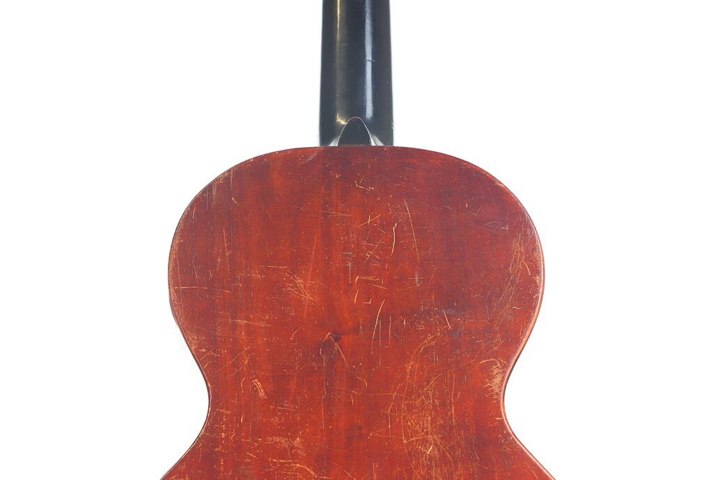 Die Rückseite der Braun & Hauser 1905 Klassische Gitarre weist ein dunkles, abgenutztes Holzfinish mit sichtbaren Kratzern und Schrammen vom starken Gebrauch auf. Nur der Korpus der Gitarre und ein Teil des Halses erscheinen vor einem weißen Hintergrund. Die Rückseite der Braun & Hauser 1905 Klassische Gitarre weist ein dunkles, abgenutztes Holzfinish mit sichtbaren Kratzern und Schrammen vom starken Gebrauch auf. Nur der Korpus der Gitarre und ein Teil des Halses erscheinen vor einem weißen Hintergrund.