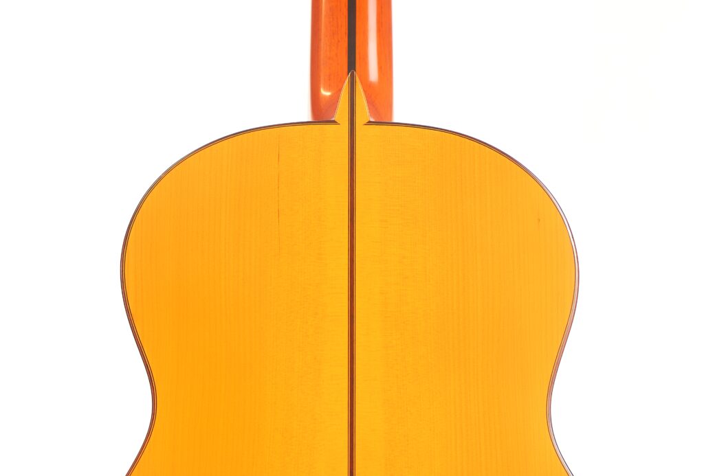 Nahaufnahme der Rückseite einer Juan Montero 1993 Blanca Flamenco-Gitarre, gelb-orangefarben, vertikal zentriert mit dem Hals oben sichtbar vor einem weißen Hintergrund. Nahaufnahme der Rückseite einer Juan Montero 1993 Blanca Flamenco-Gitarre, gelb-orangefarben, vertikal zentriert mit dem Hals oben sichtbar vor einem weißen Hintergrund.