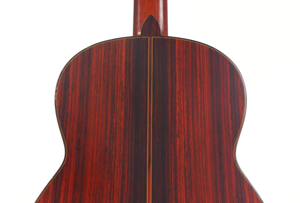 Die Rückseite der „Klassische Gitarre“ von Joachim Schneider aus dem Jahr 1977 mit glänzender Oberfläche und sattem rotbraunem Holz mit dunklen vertikalen Maserungslinien ist vor einem weißen Hintergrund fotografiert. Die Rückseite der „Klassische Gitarre“ von Joachim Schneider aus dem Jahr 1977 mit glänzender Oberfläche und sattem rotbraunem Holz mit dunklen vertikalen Maserungslinien ist vor einem weißen Hintergrund fotografiert.