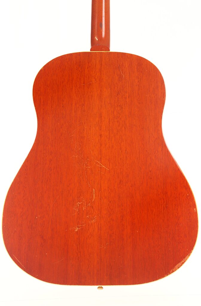 Die Rückseite einer Gibson J-50 Akustikgitarre aus dem Jahr 1952 weist eine rotbraune Lackierung mit sichtbarer Holzmaserung und leichten Kratzern auf, die sich von einem weißen Hintergrund abhebt. Die Rückseite einer Gibson J-50 Akustikgitarre aus dem Jahr 1952 weist eine rotbraune Lackierung mit sichtbarer Holzmaserung und leichten Kratzern auf, die sich von einem weißen Hintergrund abhebt.