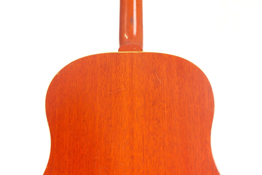 Das Bild zeigt die Rückseite der Gibson J-50 Akustikgitarre aus dem Jahr 1952 mit einer glatten, rotbraunen Holzoberfläche vor einem schlichten weißen Hintergrund. Das Bild zeigt die Rückseite der Gibson J-50 Akustikgitarre aus dem Jahr 1952 mit einer glatten, rotbraunen Holzoberfläche vor einem schlichten weißen Hintergrund.