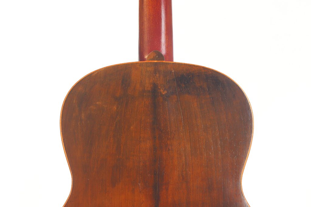 Nahaufnahme der Rückseite einer Andres Marin 1900 Klassische Gitarre, die die rötlich-braune, abgenutzte Holzoberfläche und die Mittelnaht vor einem weißen Hintergrund zeigt. Nahaufnahme der Rückseite einer Andres Marin 1900 Klassische Gitarre, die die rötlich-braune, abgenutzte Holzoberfläche und die Mittelnaht vor einem weißen Hintergrund zeigt.