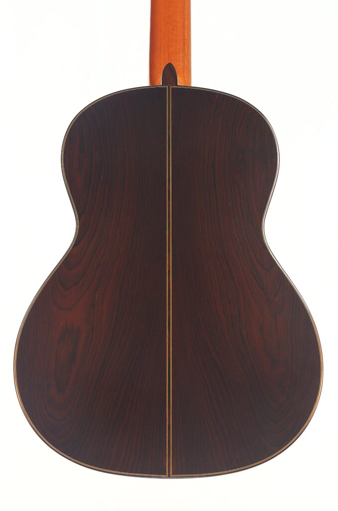 Die Rückseite einer Vicente Carrillo 1998 Torres Klassische Gitarre zeigt dunkles Holz mit einer zentralen Naht, natürlicher Holzmaserung und einem hellbraunen Hals, dargestellt vor einem weißen Hintergrund. Die Rückseite einer Vicente Carrillo 1998 Torres Klassische Gitarre zeigt dunkles Holz mit einer zentralen Naht, natürlicher Holzmaserung und einem hellbraunen Hals, dargestellt vor einem weißen Hintergrund.