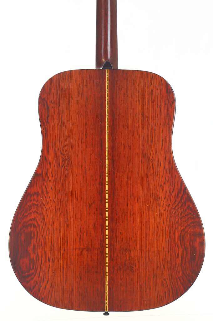 Das Bild zeigt die Rückseite einer Martin D-21 Akustikgitarre aus dem Jahr 1965. Das Holz ist rötlich-braun mit sichtbaren Maserungen und einem dekorativen gelb-schwarzen Mittelstreifen. Das Bild zeigt die Rückseite einer Martin D-21 Akustikgitarre aus dem Jahr 1965. Das Holz ist rötlich-braun mit sichtbaren Maserungen und einem dekorativen gelb-schwarzen Mittelstreifen.