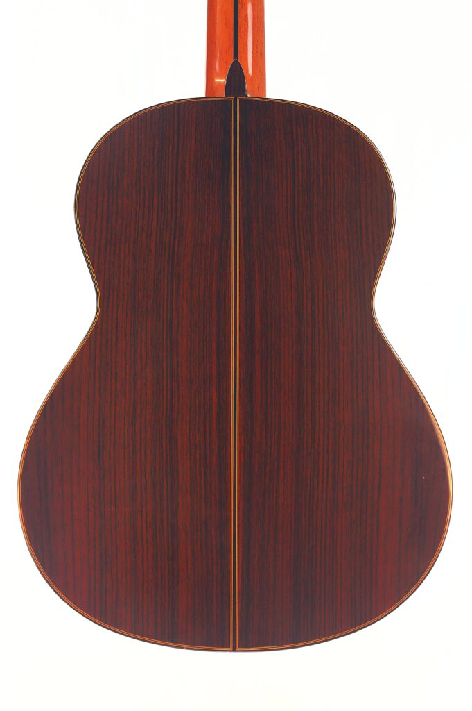 Die Rückseite der Juan Miguel Gonzalez 2006 Klassische Gitarre, mit dunkler, reicher Holzmaserung und zentraler Naht, fotografiert vor einem weißen Hintergrund. Die Rückseite der Juan Miguel Gonzalez 2006 Klassische Gitarre, mit dunkler, reicher Holzmaserung und zentraler Naht, fotografiert vor einem weißen Hintergrund.