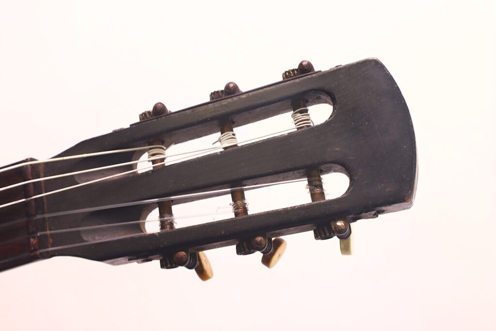 Nahaufnahme der Kopfplatte der Braun & Hauser 1905 Klassische Gitarre mit Stimmwirbeln und Saiten vor einem schlichten, hellen Hintergrund. Nahaufnahme der Kopfplatte der Braun & Hauser 1905 Klassische Gitarre mit Stimmwirbeln und Saiten vor einem schlichten, hellen Hintergrund.