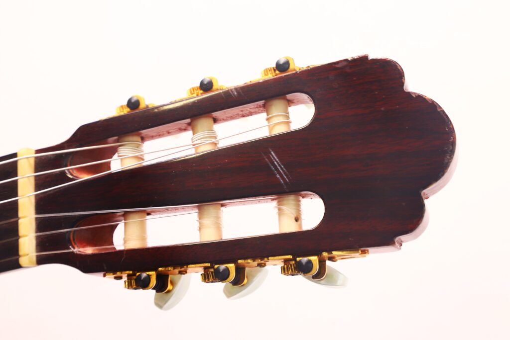 Nahaufnahme des Kopfes einer Juan Estruch Chet Atkins Yellow Label 1976 Klassische Gitarre, mit Stimmwirbeln, Saiten und Holzmaserung vor einem schlichten, hellen Hintergrund. Nahaufnahme des Kopfes einer Juan Estruch Chet Atkins Yellow Label 1976 Klassische Gitarre, mit Stimmwirbeln, Saiten und Holzmaserung vor einem schlichten, hellen Hintergrund.