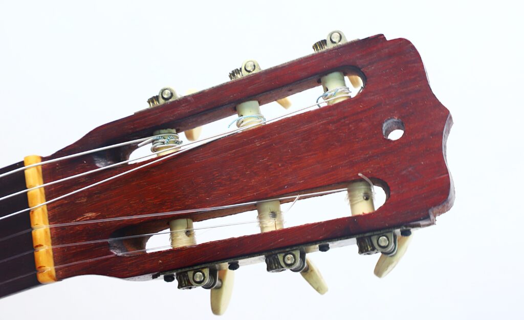 Nahaufnahme des Kopfstücks der Jose Ramirez I 1921 Klassische Gitarre, bei der die Stimmwirbel, Saiten und Holzdetails vor einem schlichten weißen Hintergrund hervorgehoben werden. Nahaufnahme des Kopfstücks der Jose Ramirez I 1921 Klassische Gitarre, bei der die Stimmwirbel, Saiten und Holzdetails vor einem schlichten weißen Hintergrund hervorgehoben werden.