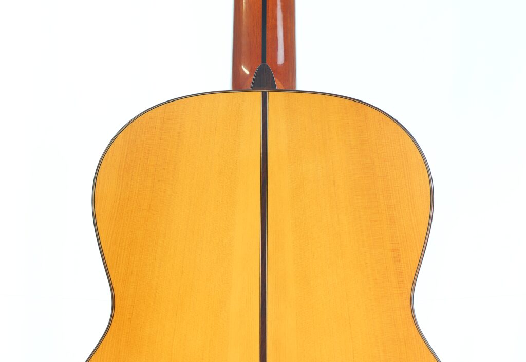 Nahaufnahme der Rückseite einer Camps Primera A 2018 Flamenco-Gitarre, die sich durch helles Holz mit einer dunklen Mittelnaht und einem nach oben verlaufenden Hals auszeichnet. Nahaufnahme der Rückseite einer Camps Primera A 2018 Flamenco-Gitarre, die sich durch helles Holz mit einer dunklen Mittelnaht und einem nach oben verlaufenden Hals auszeichnet.