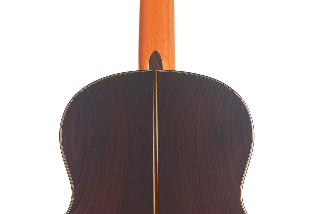 Die Rückseite einer Vicente Carrillo 1998 Torres Klassische Gitarre zeigt dunkles Holz mit einem zentralen Intarsienstreifen und einem helleren Hals, fotografiert vor einem weißen Hintergrund. Die Rückseite einer Vicente Carrillo 1998 Torres Klassische Gitarre zeigt dunkles Holz mit einem zentralen Intarsienstreifen und einem helleren Hals, fotografiert vor einem weißen Hintergrund.