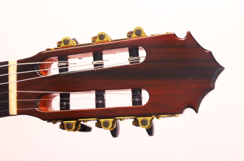 Nahaufnahme des Kopfes der José M Palmero 2023 Flamenco-Gitarre mit Holzoptik, goldenen Stimmwirbeln und drei sichtbaren Saiten vor einem schlichten, hellen Hintergrund. Nahaufnahme des Kopfes der José M Palmero 2023 Flamenco-Gitarre mit Holzoptik, goldenen Stimmwirbeln und drei sichtbaren Saiten vor einem schlichten, hellen Hintergrund.