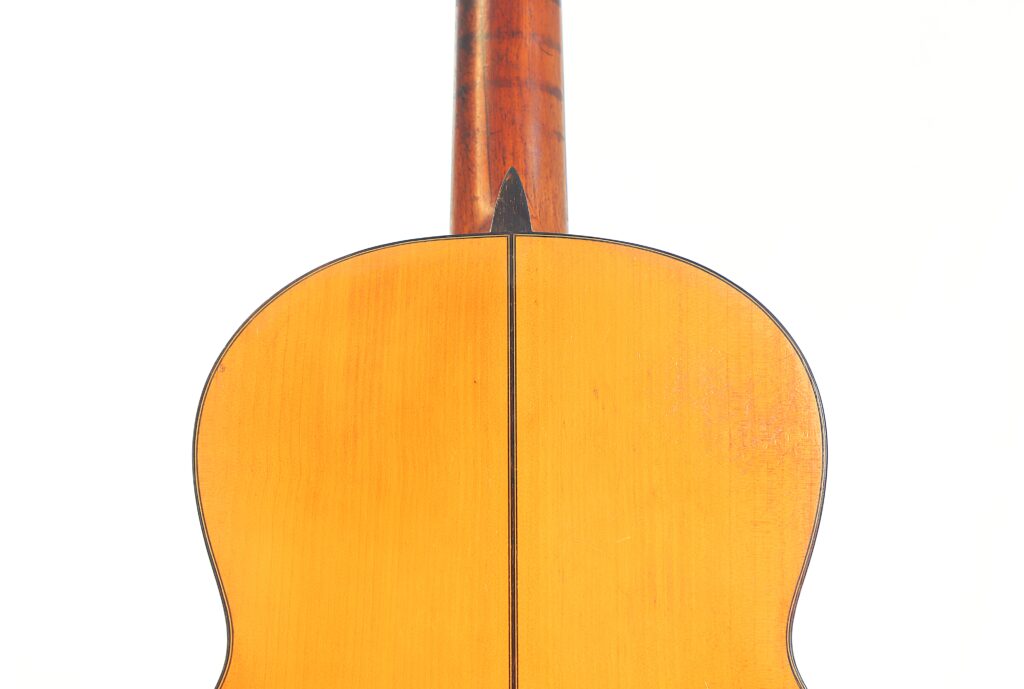 Nahaufnahme der Rückseite einer Flamenco-Gitarre von Jose Ramirez aus dem Jahr 1955. Sie zeigt eine helle Holzoberfläche mit einer dunklen Naht in der Mitte und an der Basis des Halses, vor einem weißen Hintergrund. Nahaufnahme der Rückseite einer Flamenco-Gitarre von Jose Ramirez aus dem Jahr 1955. Sie zeigt eine helle Holzoberfläche mit einer dunklen Naht in der Mitte und an der Basis des Halses, vor einem weißen Hintergrund.