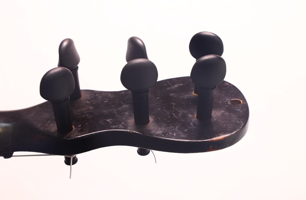 Nahaufnahme der Stimmwirbel am Kopf einer Stephan-Thumhart-Romantikgitarre von 1838 vor einem schlichten weißen Hintergrund. Das Holz wirkt abgenutzt und gealtert. Nahaufnahme der Stimmwirbel am Kopf einer Stephan-Thumhart-Romantikgitarre von 1838 vor einem schlichten weißen Hintergrund. Das Holz wirkt abgenutzt und gealtert.