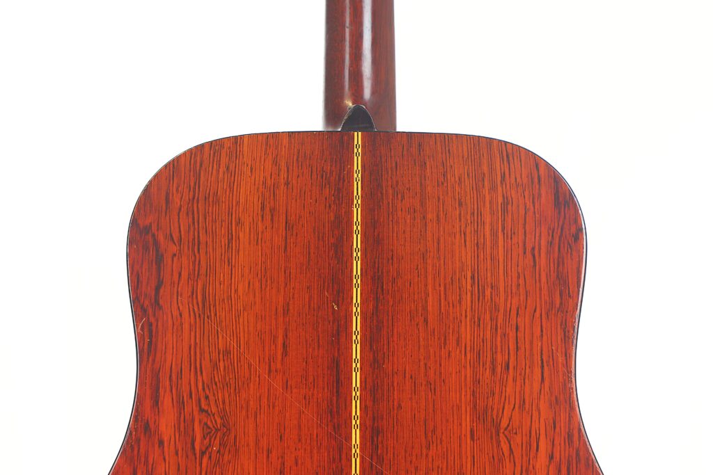 Nahaufnahme der Rückseite einer Martin D-21 Akustikgitarre aus dem Jahr 1965 mit poliertem, rotbraunem Holz mit einer dekorativen gelben Einlage in der Mitte und einer glatten, glänzenden Oberfläche. Nahaufnahme der Rückseite einer Martin D-21 Akustikgitarre aus dem Jahr 1965 mit poliertem, rotbraunem Holz mit einer dekorativen gelben Einlage in der Mitte und einer glatten, glänzenden Oberfläche.