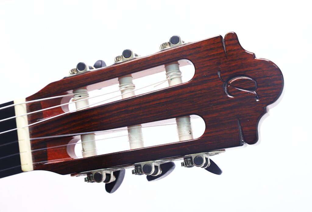 Nahaufnahme des Kopfes einer Flamenco-Gitarre der Serie „Camps Primera A 2018“ mit sichtbaren Stimmwirbeln, Saiten und Holzmaserung vor weißem Hintergrund. Nahaufnahme des Kopfes einer Flamenco-Gitarre der Serie „Camps Primera A 2018“ mit sichtbaren Stimmwirbeln, Saiten und Holzmaserung vor weißem Hintergrund.