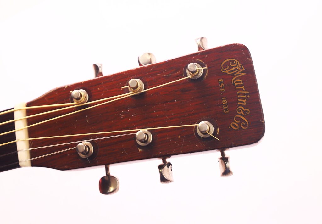 Nahaufnahme der Martin D-21 1965 Akustik Gitarre Kopfplatte mit Stimmwirbeln und Saiten, mit "Martin & Co Est. 1833" in goldener Schrift auf dem Holz. Nahaufnahme der Martin D-21 1965 Akustik Gitarre Kopfplatte mit Stimmwirbeln und Saiten, mit "Martin & Co Est. 1833" in goldener Schrift auf dem Holz.