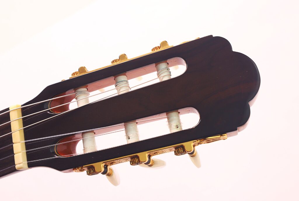 Nahaufnahme der Kopfplatte einer Vicente Carrillo 1998 Torres Klassische Gitarre mit Stimmwirbeln, weißen Saiten und goldenen Beschlägen vor einem hellen Hintergrund. Nahaufnahme der Kopfplatte einer Vicente Carrillo 1998 Torres Klassische Gitarre mit Stimmwirbeln, weißen Saiten und goldenen Beschlägen vor einem hellen Hintergrund.