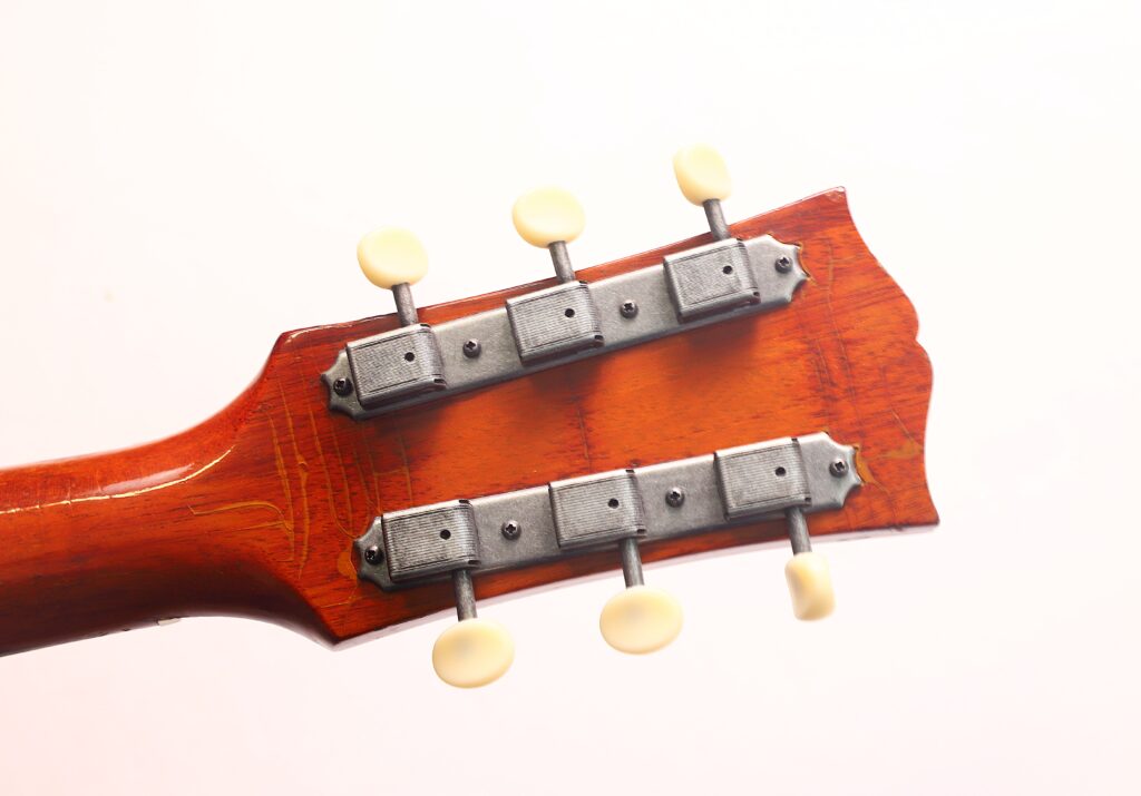 Nahaufnahme der Rückseite des Kopfes einer Gibson J-50 Akustikgitarre aus dem Jahr 1952, bei der zwei Metallplatten für die Stimmwirbel mit weißen Wirbeln vor einem schlichten, hellen Hintergrund hervorgehoben werden. Nahaufnahme der Rückseite des Kopfes einer Gibson J-50 Akustikgitarre aus dem Jahr 1952, bei der zwei Metallplatten für die Stimmwirbel mit weißen Wirbeln vor einem schlichten, hellen Hintergrund hervorgehoben werden.