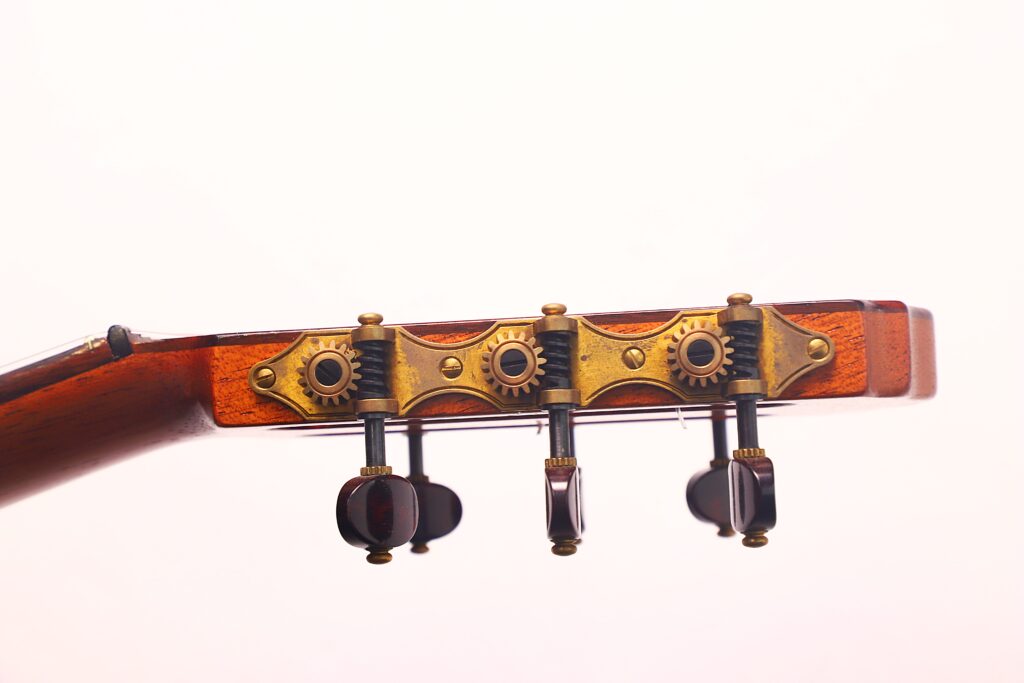 Nahaufnahme der Stimmwirbel und Messingzahnräder am Kopf einer Carl Hermann Schäfer – Nicolaus Wollf 2012 Klassische Gitarre mit Holzfinish, vor einem hellen, neutralen Hintergrund. Nahaufnahme der Stimmwirbel und Messingzahnräder am Kopf einer Carl Hermann Schäfer – Nicolaus Wollf 2012 Klassische Gitarre mit Holzfinish, vor einem hellen, neutralen Hintergrund.