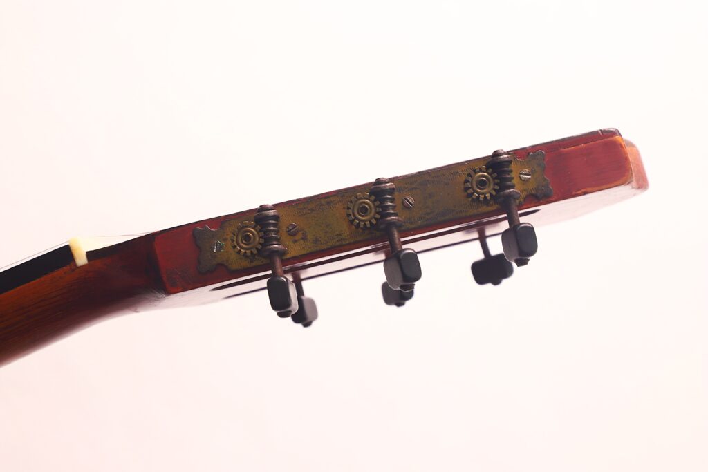 Nahaufnahme der Kopfplatte der Andres Marin 1900 Klassische Gitarre mit drei Stimmwirbeln, Metallzahnrädern und einem Teil des Holzhalses vor einem hellen Hintergrund. Nahaufnahme der Kopfplatte der Andres Marin 1900 Klassische Gitarre mit drei Stimmwirbeln, Metallzahnrädern und einem Teil des Holzhalses vor einem hellen Hintergrund.