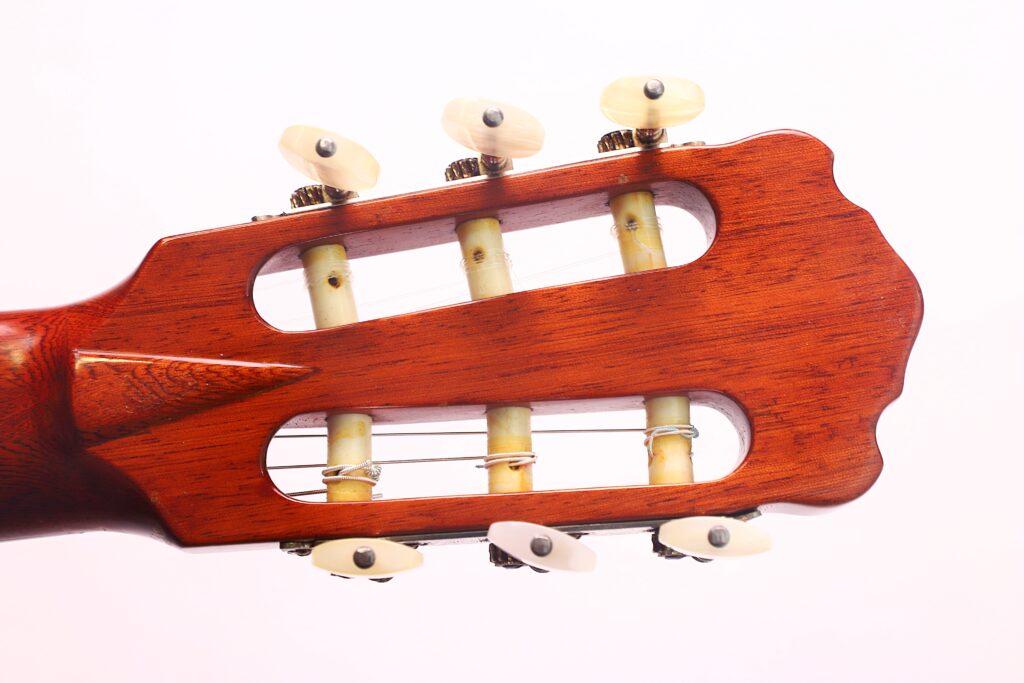 Nahaufnahme des Kopfes einer „Klassischen Gitarre“ von Joachim Schneider aus dem Jahr 1977, auf der die Stimmwirbel, die Zahnräder und die Holzoberfläche vor einem schlichten weißen Hintergrund zu sehen sind. Nahaufnahme des Kopfes einer „Klassischen Gitarre“ von Joachim Schneider aus dem Jahr 1977, auf der die Stimmwirbel, die Zahnräder und die Holzoberfläche vor einem schlichten weißen Hintergrund zu sehen sind.