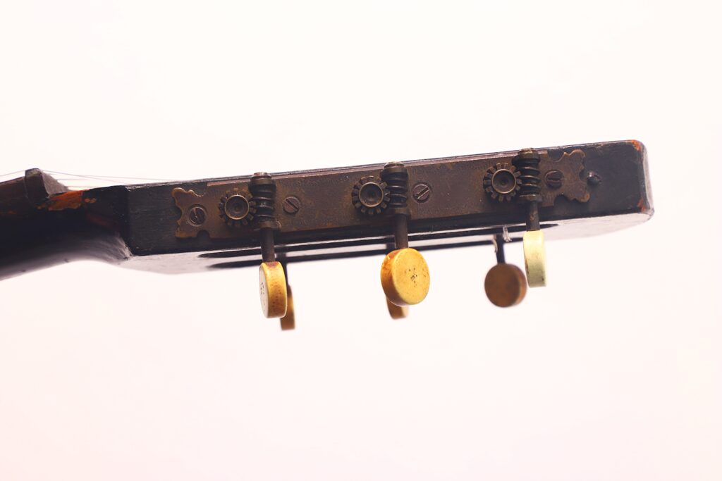 Nahaufnahme der Stimmwirbel und Zahnräder an der Kopfplatte einer abgenutzten, alten Braun & Hauser 1905 Klassische Gitarre vor einem schlichten weißen Hintergrund. Nahaufnahme der Stimmwirbel und Zahnräder an der Kopfplatte einer abgenutzten, alten Braun & Hauser 1905 Klassische Gitarre vor einem schlichten weißen Hintergrund.