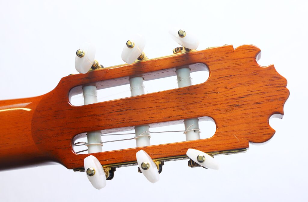 Nahaufnahme des Kopfes einer „Doble Tapa Klassische Gitarre“ von Manuel Contreras aus dem Jahr 1981 mit sechs weißen Stimmwirbeln, einer Holzoberfläche und Nylonsaiten vor weißem Hintergrund. Nahaufnahme des Kopfes einer „Doble Tapa Klassische Gitarre“ von Manuel Contreras aus dem Jahr 1981 mit sechs weißen Stimmwirbeln, einer Holzoberfläche und Nylonsaiten vor weißem Hintergrund.