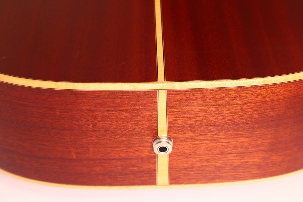Nahaufnahme der Unterkante einer Lakewood D-14-12 Cut 2005 Akustik Gitarre. Hervorzuheben sind das rötlich-braune Holz, die helle Einlage in der Mitte und der Klinkeneingang zum Anschluss eines Audiokabels. Nahaufnahme der Unterkante einer Lakewood D-14-12 Cut 2005 Akustik Gitarre. Hervorzuheben sind das rötlich-braune Holz, die helle Einlage in der Mitte und der Klinkeneingang zum Anschluss eines Audiokabels.