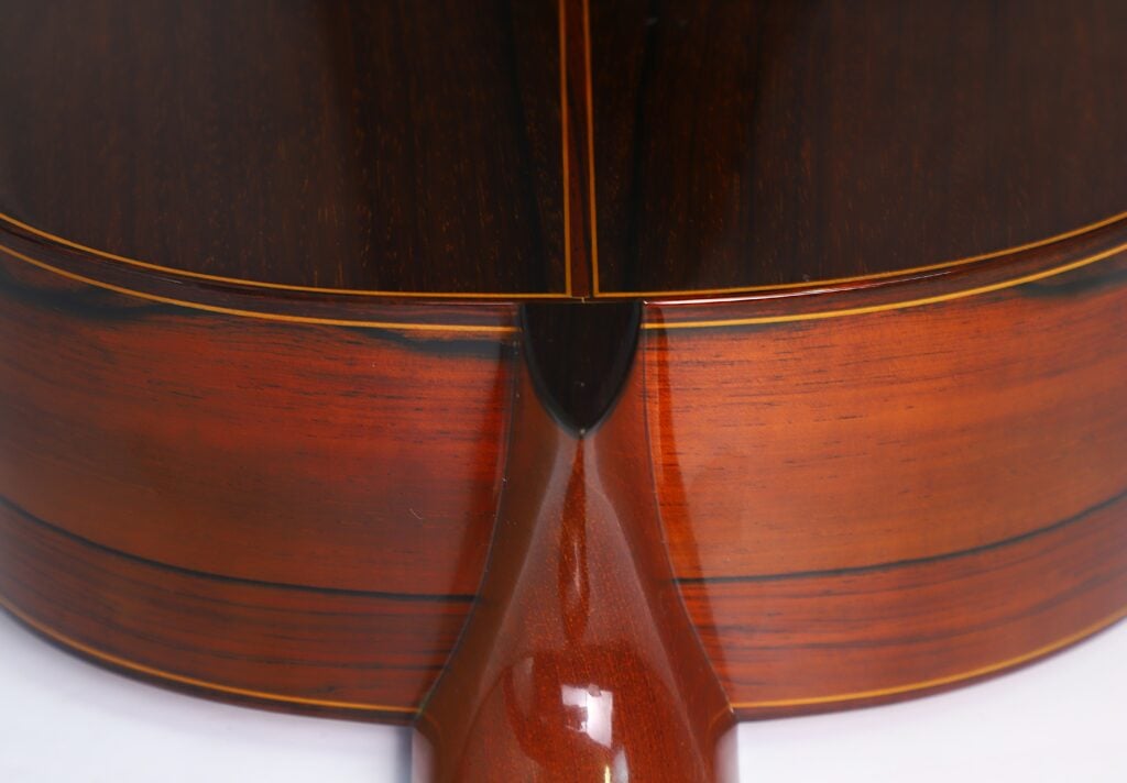 Nahaufnahme der Rückseite und der Seite einer „Doble Tapa Klassische Gitarre“ von Manuel Contreras aus dem Jahr 1981, wobei die polierte Verbindungsstelle zwischen Hals und Korpus besonders hervorgehoben wird. Das Holz besticht durch satte Brauntöne, eine feine Maserung und elegante, dunklere Akzentlinien. Nahaufnahme der Rückseite und der Seite einer „Doble Tapa Klassische Gitarre“ von Manuel Contreras aus dem Jahr 1981, wobei die polierte Verbindungsstelle zwischen Hals und Korpus besonders hervorgehoben wird. Das Holz besticht durch satte Brauntöne, eine feine Maserung und elegante, dunklere Akzentlinien.