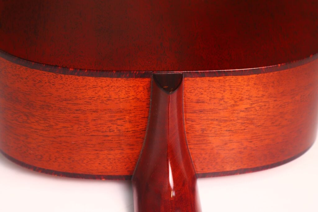 Nahaufnahme des Bodens einer Lowden S-5 Akustikgitarre. Hervorzuheben sind die glatte, hochglanzpolierte rötlich-braune Holzmaserung und die nahtlose Verbindung zwischen Hals und Korpus. Nahaufnahme des Bodens einer Lowden S-5 Akustikgitarre. Hervorzuheben sind die glatte, hochglanzpolierte rötlich-braune Holzmaserung und die nahtlose Verbindung zwischen Hals und Korpus.