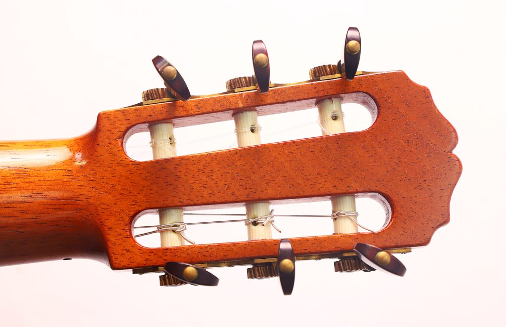 Nahaufnahme des Kopfes der „Carl Hermann Schäfer – Nicolaus Wollf 2012 Klassische Gitarre“ mit sechs Stimmwirbeln, Nylonsaiten und einer Holzoberfläche vor einem schlichten weißen Hintergrund. Nahaufnahme des Kopfes der „Carl Hermann Schäfer – Nicolaus Wollf 2012 Klassische Gitarre“ mit sechs Stimmwirbeln, Nylonsaiten und einer Holzoberfläche vor einem schlichten weißen Hintergrund.
