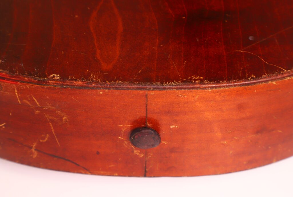Nahaufnahme einer Braun & Hauser 1905 Klassische Gitarre, die den abgenutzten, rötlich-braunen Holzkorpus mit einer runden Kante, sichtbaren Kratzern und einem dunklen Mittelknauf auf der gealterten Oberfläche zeigt. Nahaufnahme einer Braun & Hauser 1905 Klassische Gitarre, die den abgenutzten, rötlich-braunen Holzkorpus mit einer runden Kante, sichtbaren Kratzern und einem dunklen Mittelknauf auf der gealterten Oberfläche zeigt.